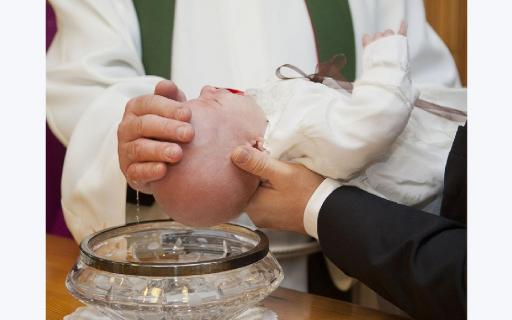Prästens hand öser vatten över ett barns huvud vid en kristallskål med guldkant.