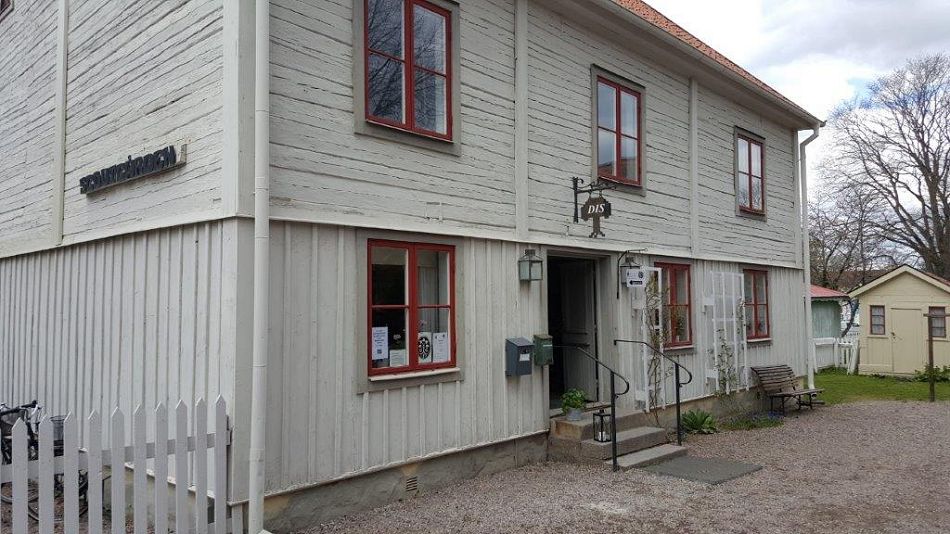 Ett vitt gammal hus med röda fönsterbågar och två våningar och källare med en skylt med namnet DIS och Scoutkårens ljusramp på ena väggen.