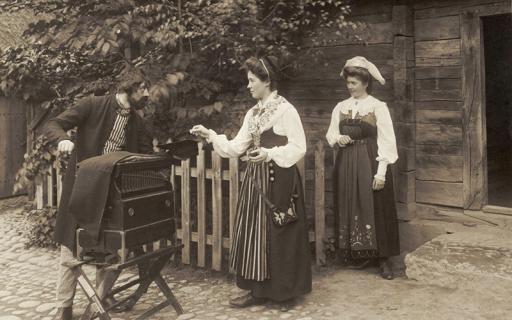 En positivhalare tar emot ett mynt av en folkdräktsklädd kvinna. Skansens vårfest 1905. Nordiska Museet.