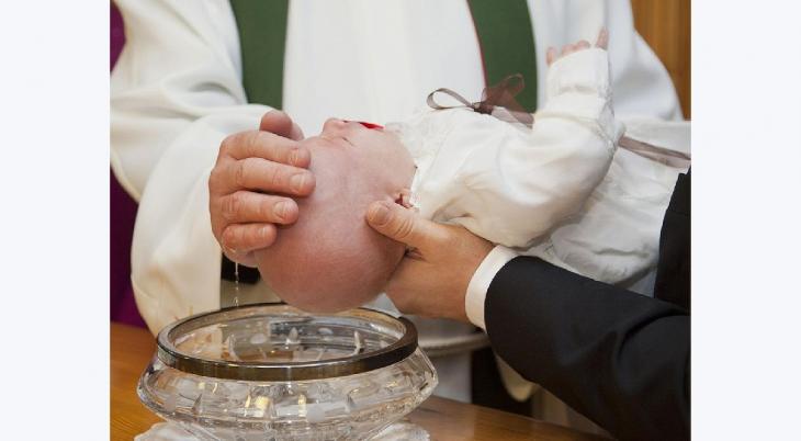 Prästens hand öser vatten över ett barns huvud vid en kristallskål med guldkant.