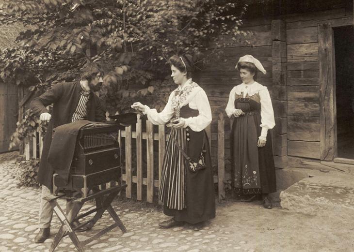 En positivhalare tar emot ett mynt av en folkdräktsklädd kvinna. Skansens vårfest 1905. Nordiska Museet.